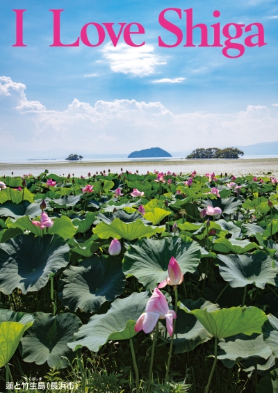 縦長の写真：美しい青空の下、水平線の向こうに島が見える。手前には蓮が一面に生えており、蓮の花のつぼみをつけている。写真の上部にピンクの大きいアルファベットで「I Love Shiga」。左下に「蓮と竹生島（長浜市）」